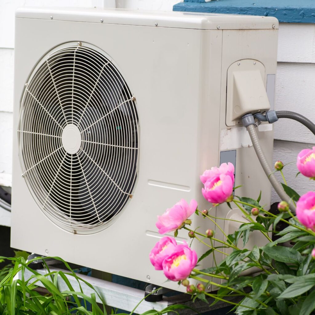 heat pump in a garden next to small pink flowers