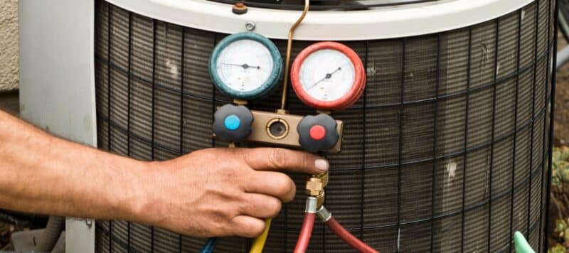 red and blue pressure gauges hanging on the edge of an outdoor ac unit