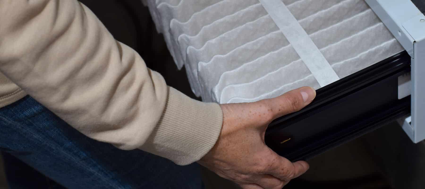closeup of an hvac technician inserting a new and clean air filter into the furnace system of a farmington new mexico home