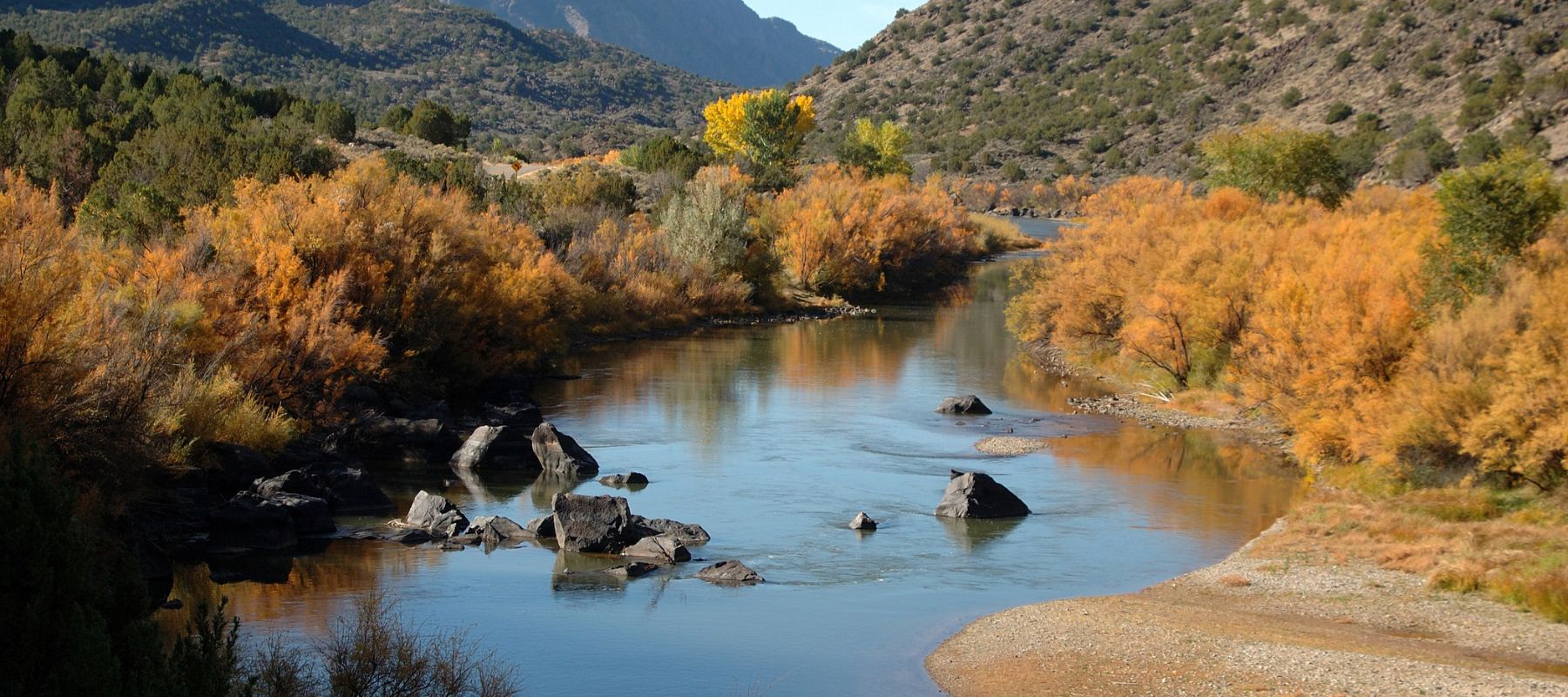 Scenic river flowing through a mountainous desert landscape with autumn-colored trees along the banks
