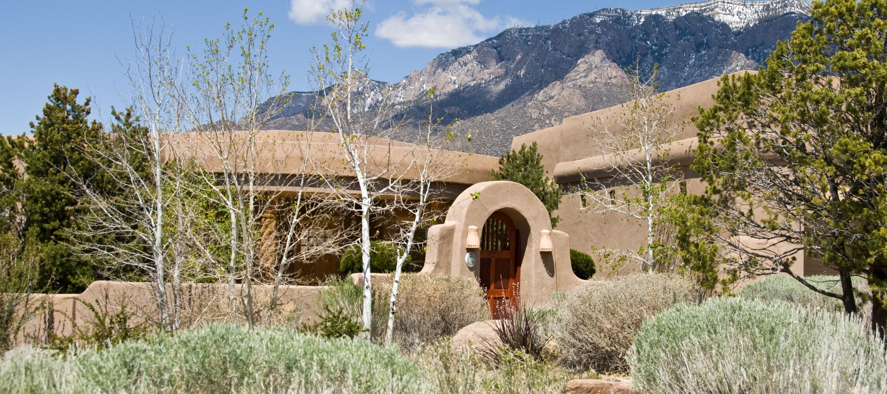 Southwestern-style adobe home surrounded by desert plants, set against a backdrop of mountains