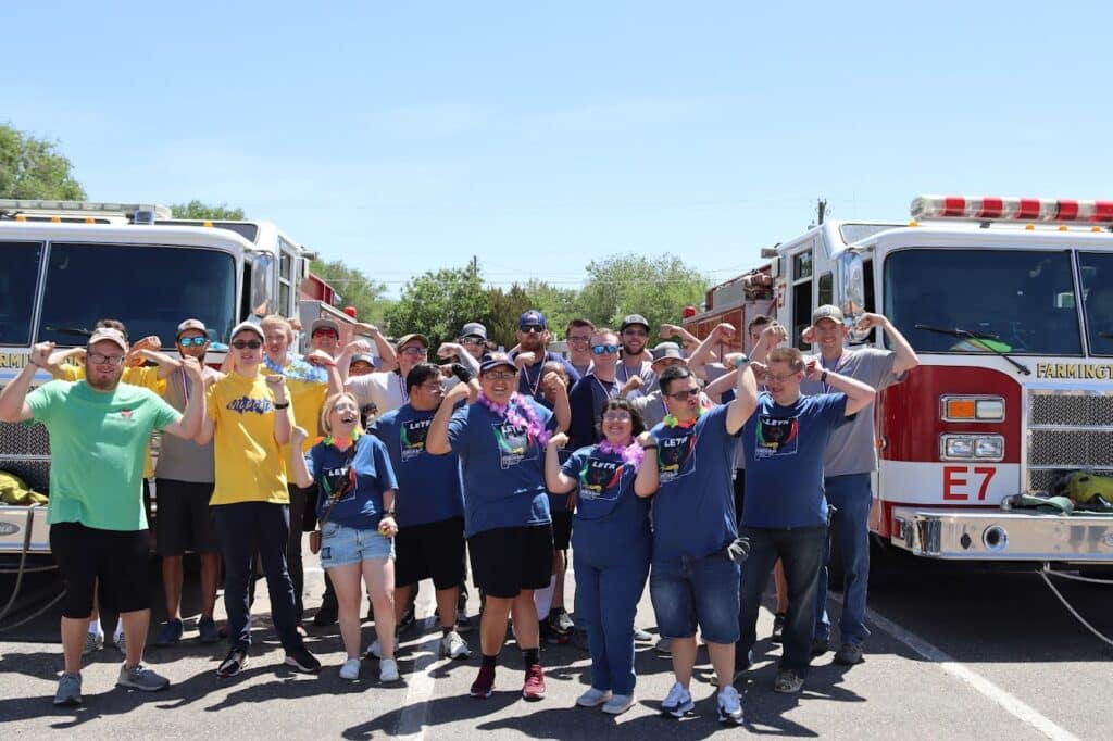 A diverse group of people flexing their arms in front of two fire trucks, showing team spirit and community involvement