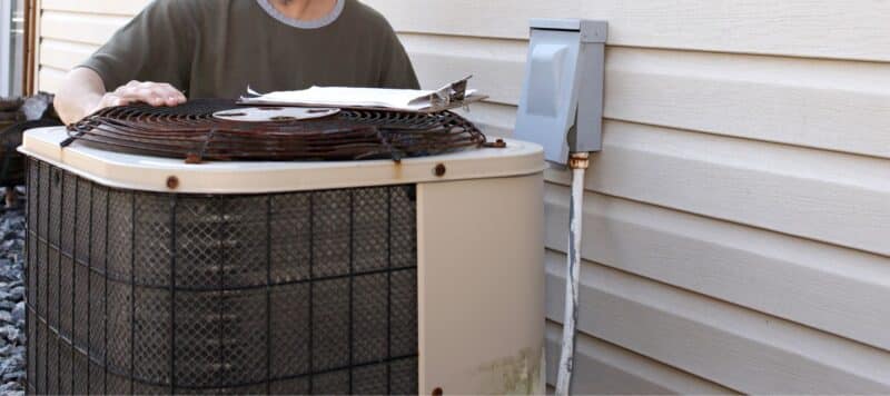 Technician inspecting an old outdoor air conditioning unit next to a house