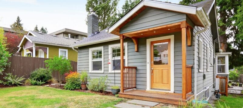 exterior of a gray home with a wood front porch and bushes in the yard