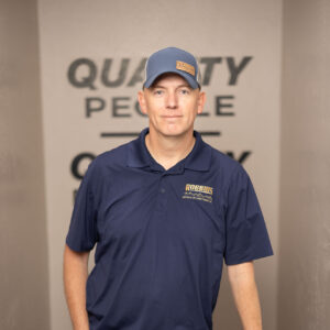 A man wearing a blue polo shirt and cap, both with the ARROWS logo, stands indoors next to an HVAC unit. The background features the partially visible words QUALITY PEOPLE on the wall.